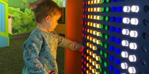 A young boy plays with lighted pegs mounted on a dark wall.
