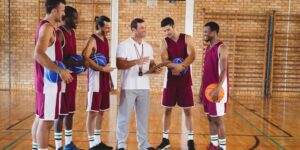 A coach and his players stand in a gym discussing plays.