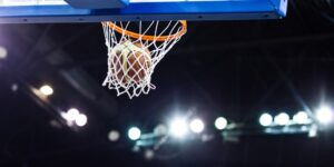 A basketball hoop with a basketball in the net. Bright lights are in the background.
