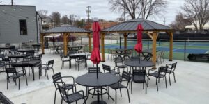 A patio with umbrella tables and chairs with pickleball courts in the background.