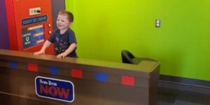 A young boy stands at a play broadcasting desk in a pretend studio.