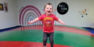 A young boy in a red t-shirt bounces on a large red-and-green inflatable.
