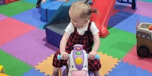 A toddler girl sits on a riding toy unicorn at a play center.