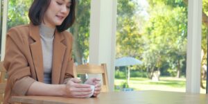 A woman sits at a table with a cup of coffee in a screened porch.
