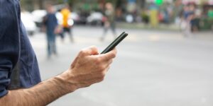 Close-up of a hand holding a smartphone with a street in the background.