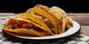 Several tacos sit fanned across a white plate on a table.