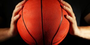 Close-up of a basketball held by two hands with a dark background.