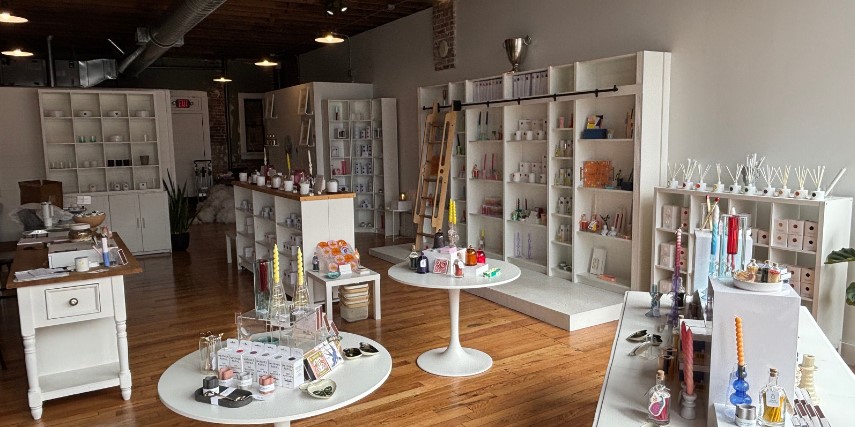 View of the inside of a candle and scents store with gleaming wood floors and clean white shelves.