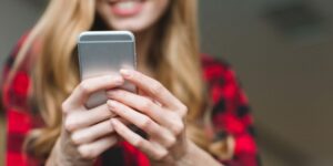 A woman in a black-and-red plaid shirt holds a phone in both hands.