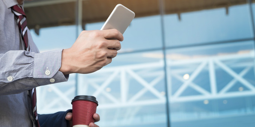 A person walks with a to-go cup of coffee, holding their phone up to look at the screen.