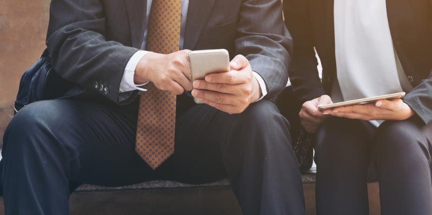 Close-up of two professionally dressed men looking at something on their devices together.