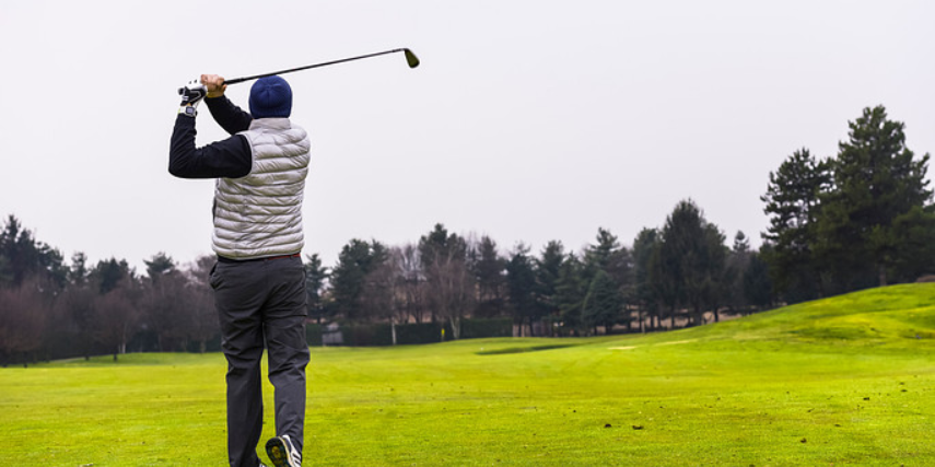 A golfer stands in full swing after driving a ball up the fairway.
