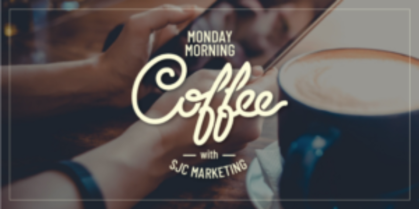 A hand grips the handle of a foamy cup of coffee with the words "Monday Morning Coffee with SJC Marketing."