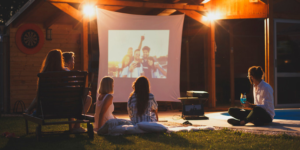 Friends sit watching a makeshift outdoor movie projected on a sheet.