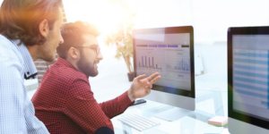 Two employees sit at monitors discussing analytics.