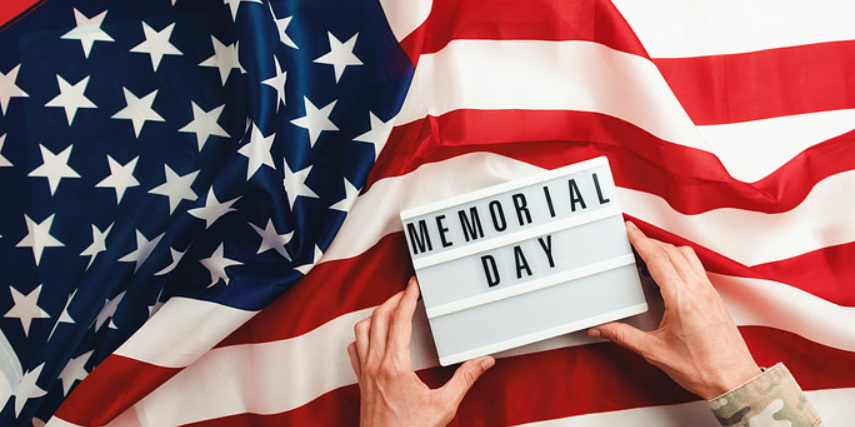 A light box with the words, "Memorial Day," is held by hands over an American flag.