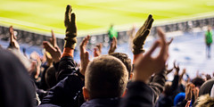 Arena football fans viewed from behind as they cheer for their teams.