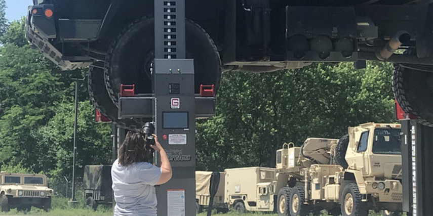 A photographer takes photos of a diesel truck up on an outdoor lift.