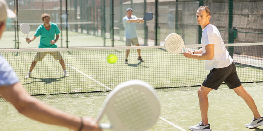 Four people play pickleball with white paddles on a green court.