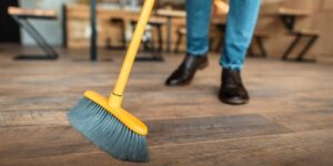A yellow and gray broom sweeps across a wood floor with a person behind it presumably holding the broom.