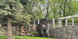 Corner of a historic stone wall in a park, surrounded by trees and greenery.