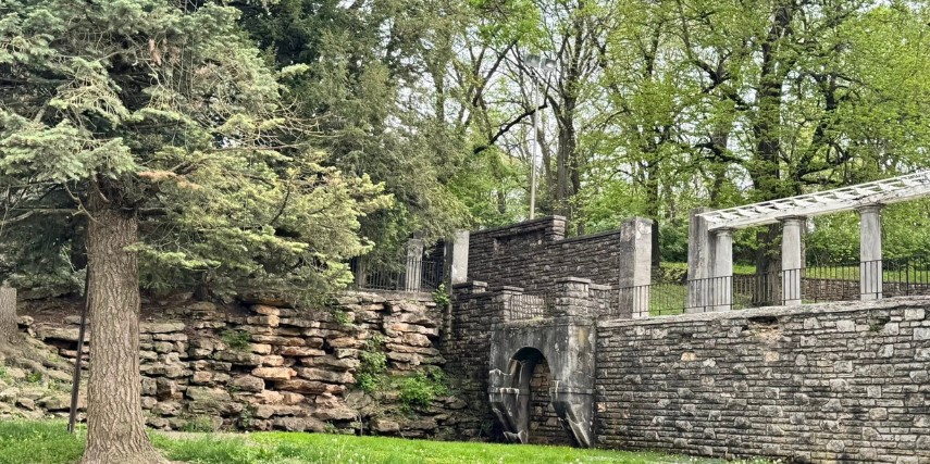 Corner of a historic stone wall in a park, surrounded by trees and greenery.