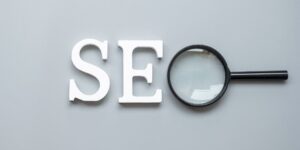 "SEO" in bold white letters against a gray background, except the "O" is a magnifying glass.