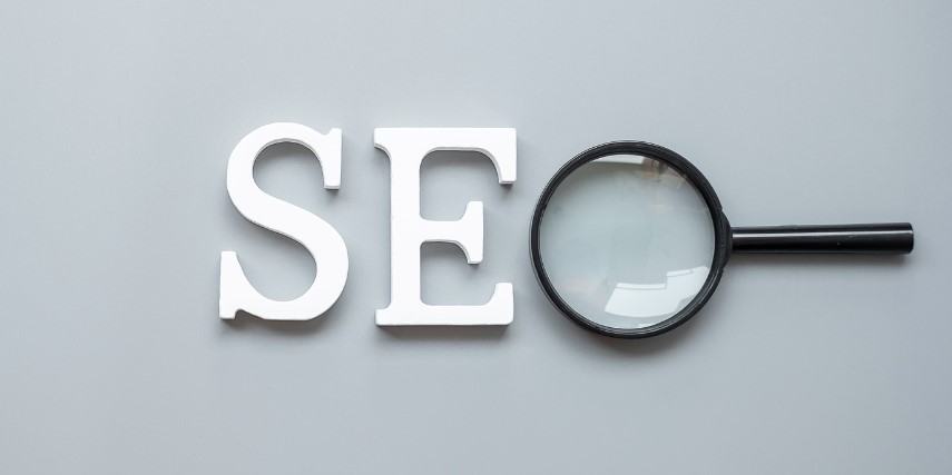 "SEO" in bold white letters against a gray background, except the "O" is a magnifying glass.