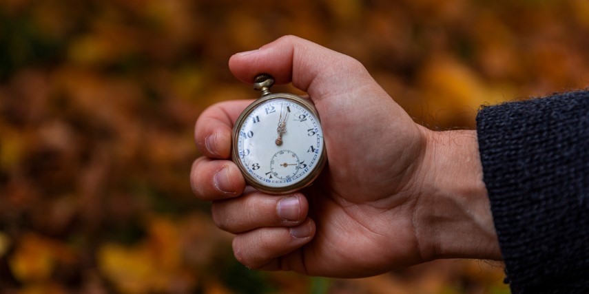 A hand holds a stopwatch against a backdrop of autumn leaves. 