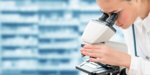 A woman in a lab looks through a microscope.