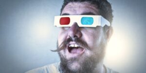 A man with a handlebar moustache has a surprised look on his face and is wearing 3D glasses.