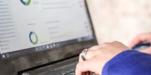 Close-up of a hand with a bold silver ring typing on a laptop.