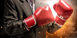 A man in a suit wears shiny red boxing gloves with explosive light in the background.