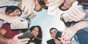 A circled group of Millennials pictured from below smiling at their smartphones.