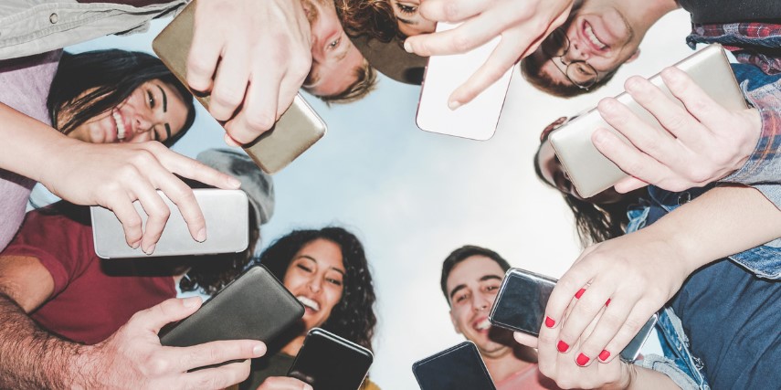A circled group of Millennials pictured from below smiling at their smartphones. 
