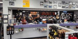 Three Lanham Music employees discuss business behind the counter, surrounded by instruments.