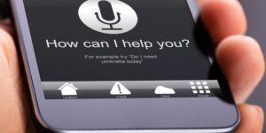 Close-up of a smartphone screen showing a microphone and the words, "How can I help you?" for voice search.