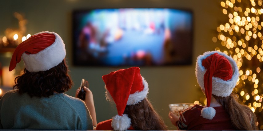 View of family from behind as they watch a holiday movie by their Christmas tree.
