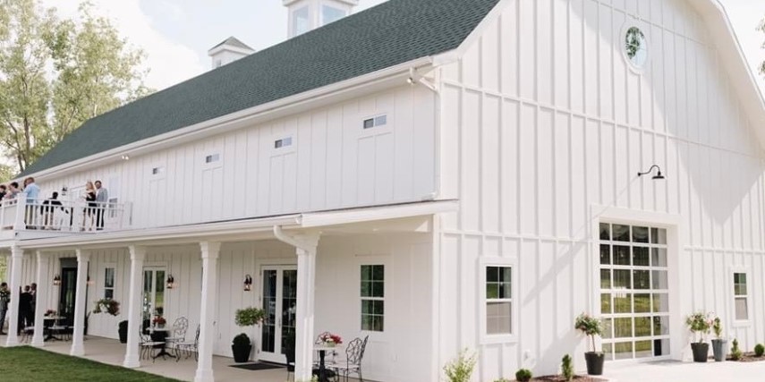 Outdoor view of a large white barn with a grey roof and a balcony.