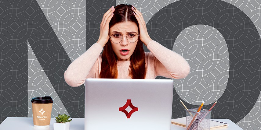 A woman sits at a desk with the word "No" across the backdrop. She's holding her hands to her head in frustration and has an overwhelmed look on her face.