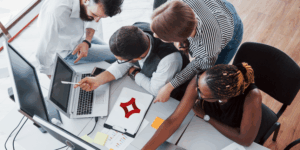 A group of coworkers gathers around a desk to look at social media marketing options.