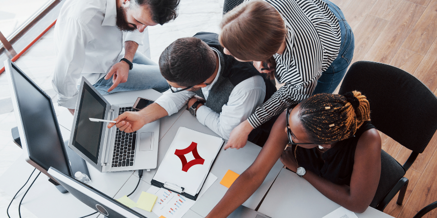 A group of coworkers gathers around a desk to look at social media marketing options.