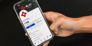 A hand holds a smartphone featuring the social media profile page for SJC Marketing.