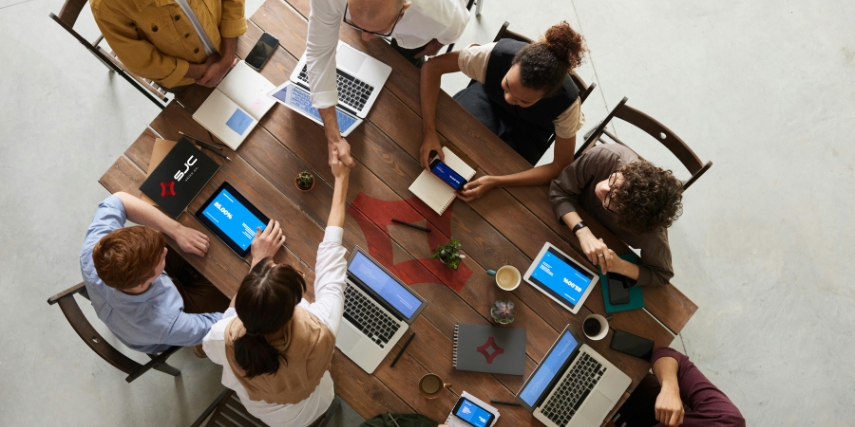 A group of people is seated around a conference table discussing plans. Two of the people are shaking hands.