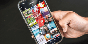 A hand holds a phone showing a grid of pictures online.