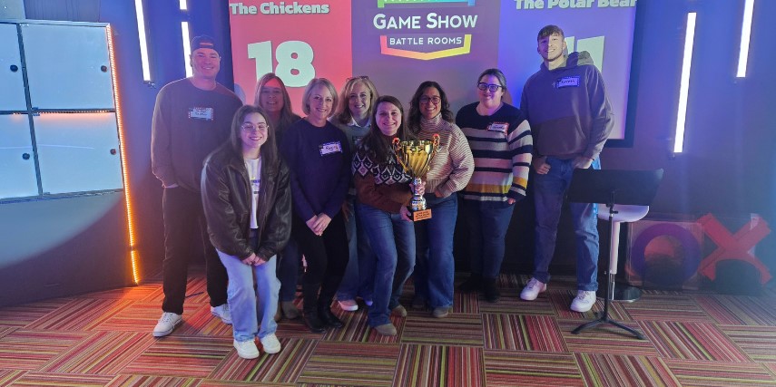 The team from SJC Marketing is posed in front of a large lighted backdrop. One person is holding a large trophy.