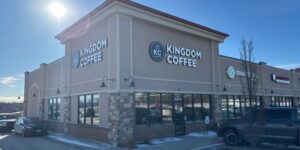 Exterior view of a coffee shop. It is painted beige and has beige stonework with the shop name in white.