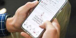 Two hands hold a smartphone showing a social media post by SJC Marketing.