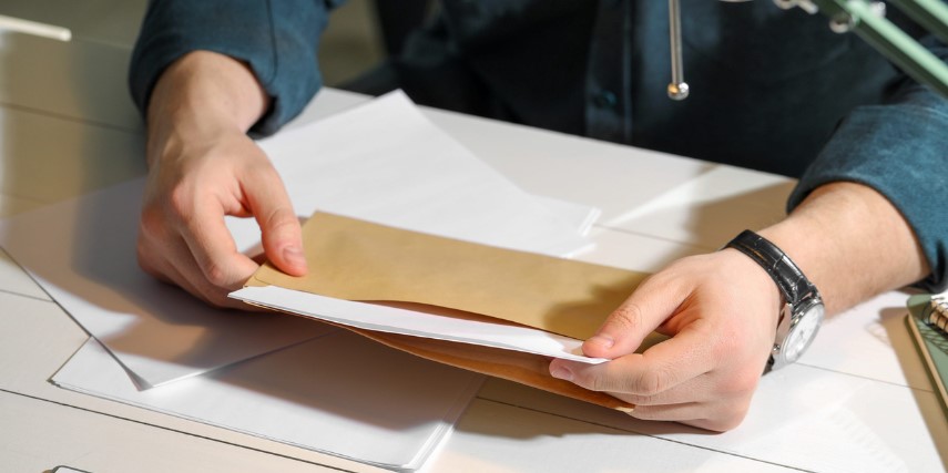 A person sits at a desk opening mail and holds a brown envelope open.