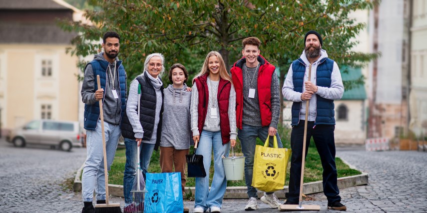 A group of volunteers poses on a street with bags and brooms.